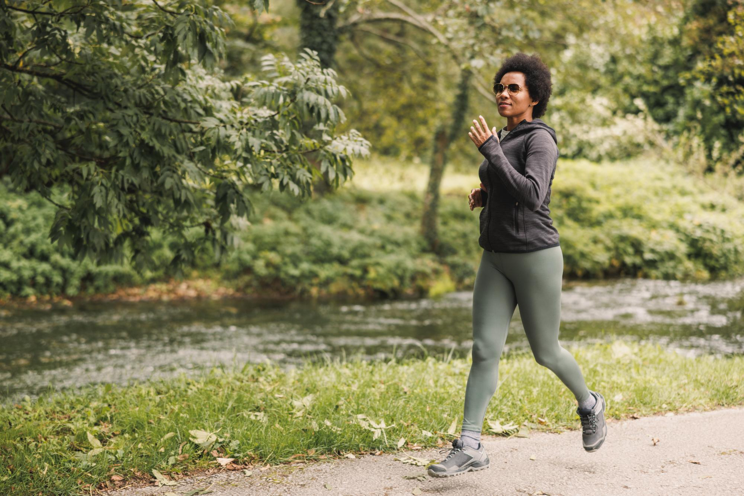 beautiful smiling mature african american woman is running along trail near mountains river nature
