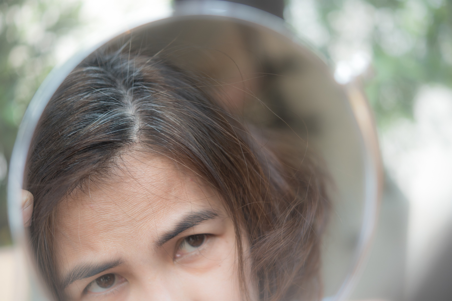 middle aged woman looking at her hair in a mirror