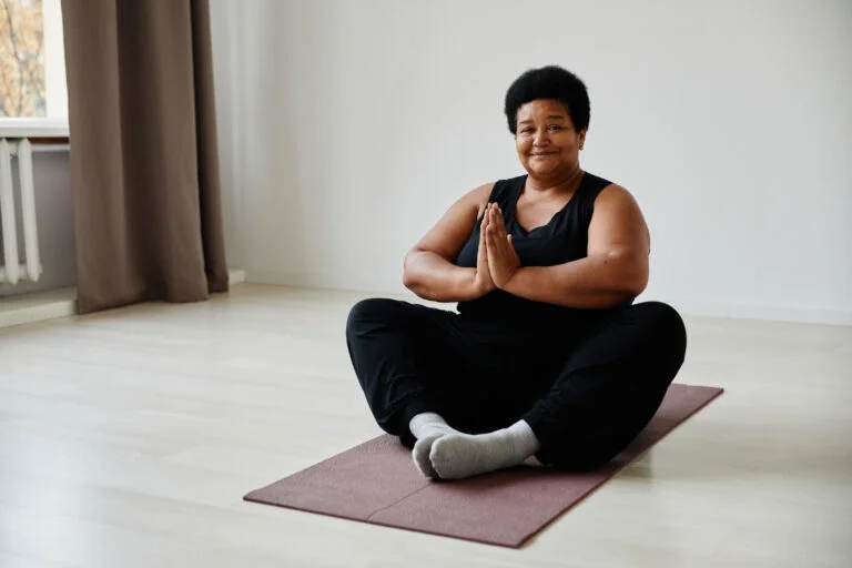 minimal full length portrait active senior woman sitting lotus position while enjoying yoga indoors smiling camera